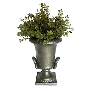 May include: A silver metal urn with a square base and ornate details. The urn is filled with a green leafy plant.