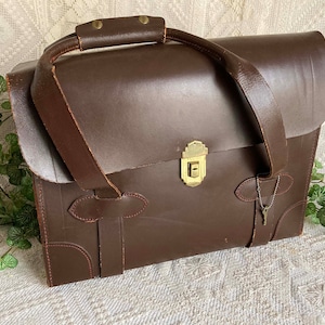 May include: A brown leather briefcase with a brass lock and key. The briefcase has two straps and a handle.