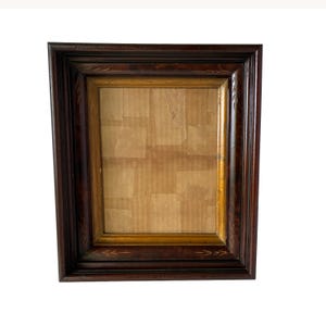 May include: A rectangular picture frame featuring a dark brown wood outer border with subtle etched arrow patterns and a contrasting inner gold-toned trim. The center of the frame is filled with a light brown cardboard backing material.