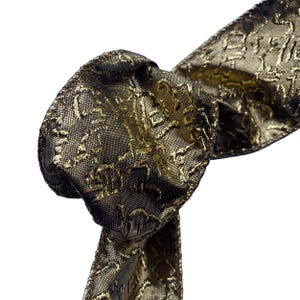 Könnte beinhalten: Nahaufnahme einer dekorativen Schleife aus einem gold-schwarz gemusterten Band. Das Band hat eine strukturierte Oberfläche mit einem sich wiederholenden Design. Die Schleife ist geknotet, wobei die Enden des Bandes sichtbar sind.
