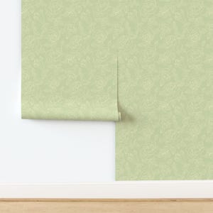 以下が含まれることがあります： 淡い緑色の背景に、クリーム色のバラの輪郭が繰り返されるパターンの壁紙ロール。 壁紙は部分的に広げられており、パターンと質感が現れています。 花柄のデザインは、エレガントさを添えています。