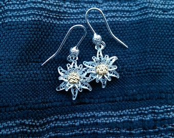 May include: A pair of silver earrings with a delicate filigree design in the shape of a white flower with a gold center.