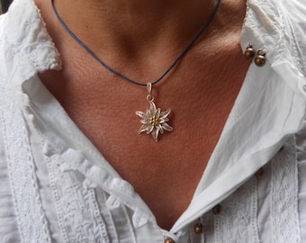 May include: A silver and gold Edelweiss pendant necklace on a blue cord. The pendant is a delicate filigree design.