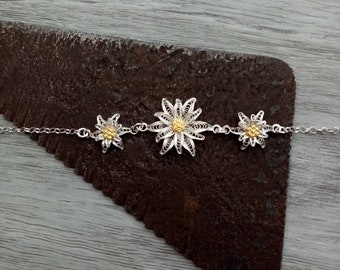 May include: A silver bracelet with three delicate flower charms. The flowers are made of filigree and have a gold center.