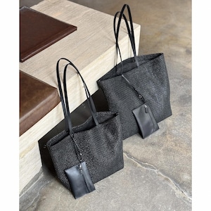 May include: Two black woven tote bags with long, thin handles. Each bag has a small, matching pouch attached. The bags are made of a textured material and are displayed on a neutral surface.