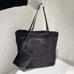 May include: Black woven tote bag with long shoulder straps and a small matching pouch. The bag has a rectangular shape and a textured, open weave design. The pouch is smooth and rectangular.