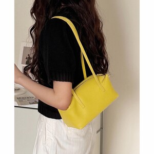May include: A bright yellow rectangular handbag with a zipper closure and long straps. The bag is made of a textured material and is being carried over the shoulder. The bag is a vibrant accessory.
