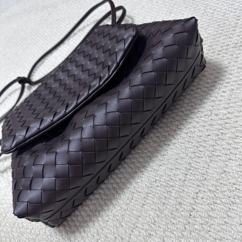 May include: A dark brown leather crossbody bag with a woven pattern. The bag has a rectangular shape with a flap closure and a long, thin strap. The leather appears to be soft and supple.