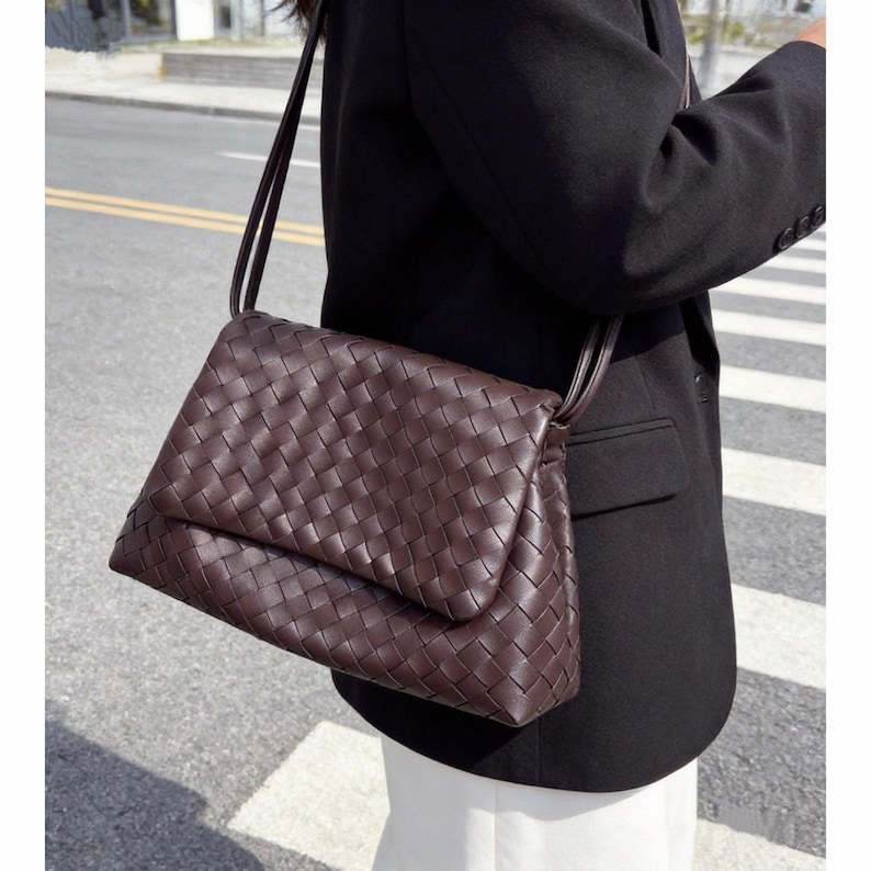 May include: A brown crossbody bag with a woven design. The bag has a rectangular shape with a flap closure and a long, thin strap. The bag is made of a dark brown material.