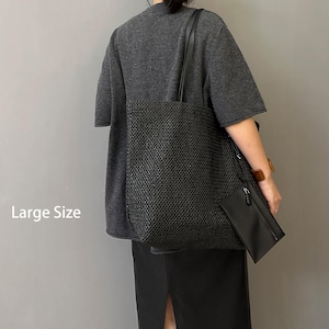 May include: A large black tote bag with a woven texture, featuring a matching small pouch. The bag has long shoulder straps and is held by a person wearing a gray top and black skirt. The text "Large Size" is visible.