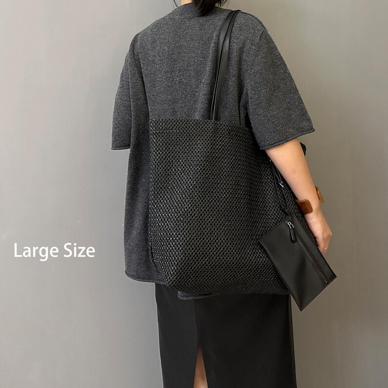 May include: A large black tote bag with a woven texture, featuring a matching small pouch. The bag has long shoulder straps and is held by a person wearing a gray top and black skirt. The text "Large Size" is visible.