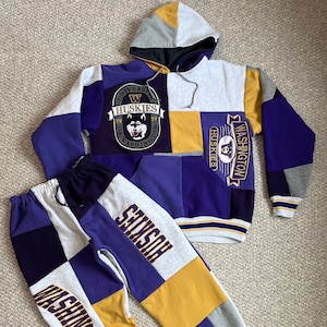 May include: A purple and yellow patchwork hoodie and sweatpants set with the University of Washington Huskies logo and the word "Huskies" on the hoodie and sweatpants.