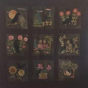 May include: A dark fabric quilt featuring nine square panels arranged in a grid. Each panel displays appliqued scenes including black birds, flowers, trees, a house, and a moon, all rendered in muted earth tones against a solid dark background.