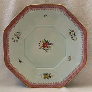 May include: An octagonal ceramic plate with a pale mint green center featuring a central floral bouquet of red, yellow, and purple flowers. The wide rim has a pink geometric lattice pattern with a gold edge and small floral sprigs.