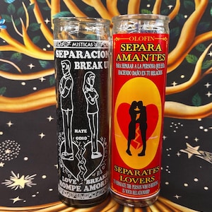May include: Two glass candles with labels. One is black with white text and illustrations of a broken heart and figures. The other is red with yellow accents, a heart, and figures. Text includes "Break Up" and "Separates Lovers."