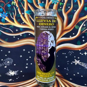 May include: A clear glass candle with the text "OLOFIN - LLUVIA DE DINERO" and "SHOWER OF MONEY". The candle features an illustration of a person with their arms raised, surrounded by falling money. The background is a tree design.