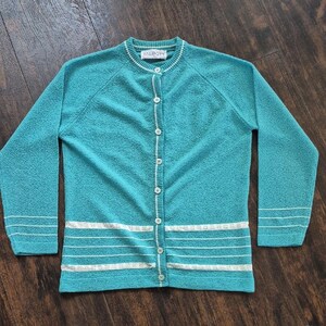 May include: A teal cardigan with white trim and buttons. The cardigan has long sleeves and a round neckline. The brand name "TALBOTS" is visible on the neckline. The bottom of the cardigan has white horizontal stripes.