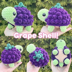 May include: A plush crochet turtle toy featuring a light green head and limbs with a textured, deep purple grape-shaped shell. The shell is topped with small green leaves. The text Grape Shell! is displayed in white letters with a pink outline.