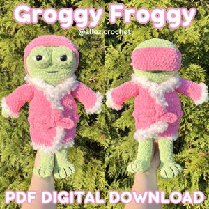 May include: A crochet frog plushie wearing a pink bathrobe with white faux fur trim. The frog has light green skin and black eyes. One version shows the frog with a pink headband, while the other shows it with a pink eye mask. Text reads Groggy Froggy.