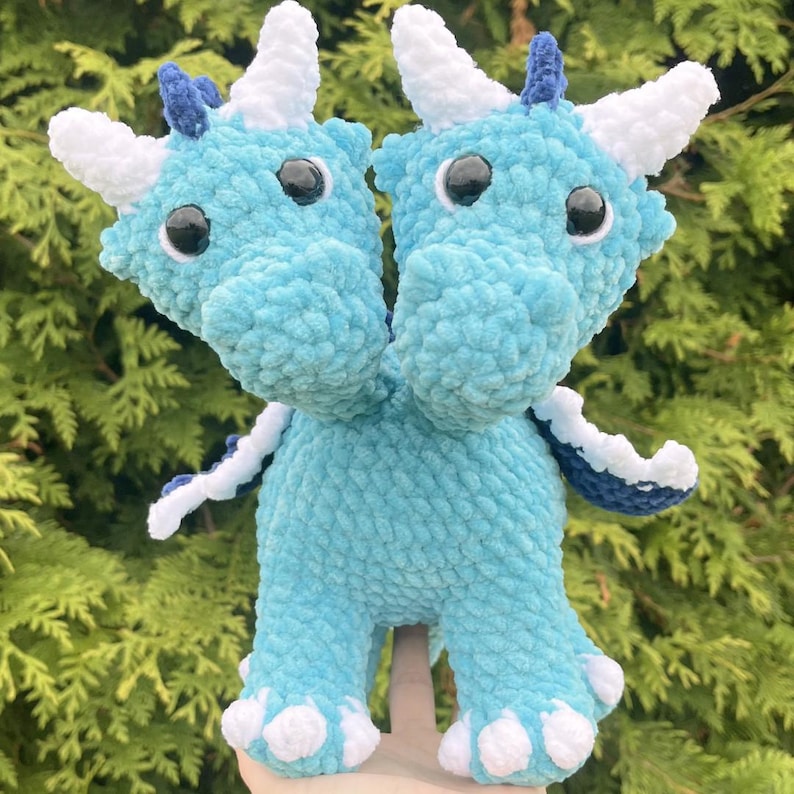 May include: A handmade, two-headed dragon plushie in shades of light blue. The dragon has white horns, white claws, and black eyes. The plushie is made of a soft, textured material, perfect for a child's toy or a unique decorative item.