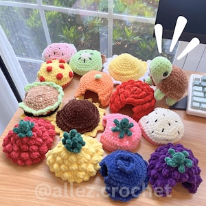 May include: A collection of small, plush, crocheted items shaped like various fruits, vegetables, and a turtle. The items feature textures in colors including red, yellow, orange, green, blue, purple, and brown. The text @allez.crochet is visible.