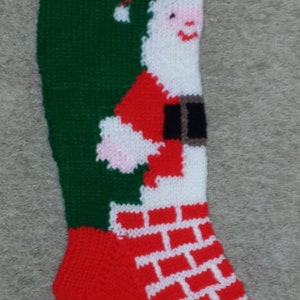 May include: A red and green knitted Christmas stocking with a white Santa Claus design. The stocking has the word "BE" knitted into the top.