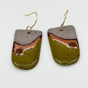 May include: A pair of dangle earrings featuring U-shaped ceramic pendants with a glossy finish. The surface displays a speckled grey top section, a metallic copper middle band, and a solid olive green bottom section, attached to gold-tone hooks.