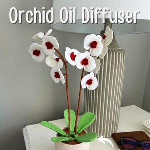 Op de afbeelding: Witte orchideeën-oliediffuser met rode centra op de bloemen. De bladeren draaien om de geur te verspreiden. Orchideeën-oliediffuser.