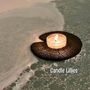 Puede incluir: Una vela de té encendida descansa sobre una hoja de nenúfar verde oscuro texturizada flotando en el agua. El agua está llena de burbujas y las palabras "Candle Lillies" están escritas en texto blanco.