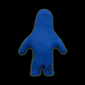 May include: A solid blue, abstract figure with a rounded head, outstretched arms, and a small base. The figure has a smooth texture and is set against a black background. The artist's signature is visible on the lower right.