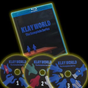 Puede incluir: Una caja de Blu-ray y tres DVD con el título "KLAY WORLD The Komplete Series". Los discos están numerados 1, 2 y 3, y tienen gráficos coloridos. La caja de Blu-ray es negra con texto azul y un borde azul.