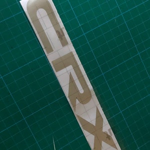 May include: A gold vinyl sticker with the word "SUBARU" written in a stylized font.