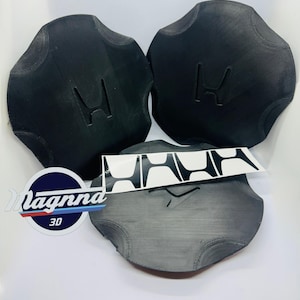 Puede incluir: Tres tapacubos de coche negros y circulares con el logotipo de Honda en relieve. También hay una pegatina con el logotipo de Honda. Los tapacubos están dispuestos sobre una superficie blanca.