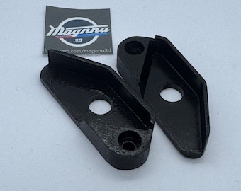 May include: Two black, 3D-printed brackets with a curved design and a circular hole. The brackets are angled and have a flat base. A small label with the text "Magnna 3D" is visible in the background.