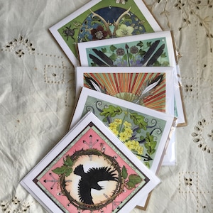 May include: A selection of art cards with nature-themed illustrations. The cards display detailed drawings of antlers, feathers, flowers, and a crow within a thorned circle. Each card has a unique design with a mix of colours and intricate details.