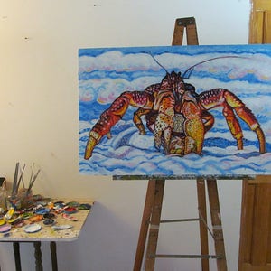 May include: A colorful painting of a large red and orange crab on a blue and white background. The crab is walking on a sandy beach with clouds in the sky. The painting is on an easel in an art studio.