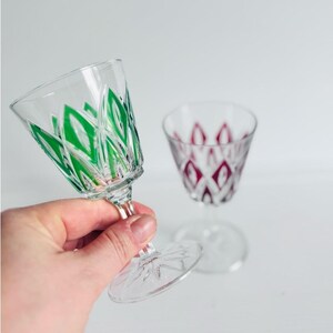 Peut inclure: Deux verres à pied transparents avec tige et base. L'un des verres présente un motif en forme de losange vert taillé dans le verre, tandis que l'autre présente un motif en forme de losange magenta. Les deux verres ont un motif étoilé sur la base.
