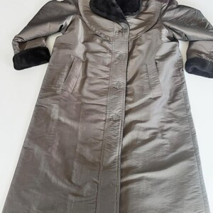 Peut inclure: Un long manteau gris métallisé doté d'un col en fausse fourrure noire et de poignets en fausse fourrure assortis. Le manteau présente une fermeture boutonnée à l'avant avec quatre boutons carrés, des manches longues et deux poches.