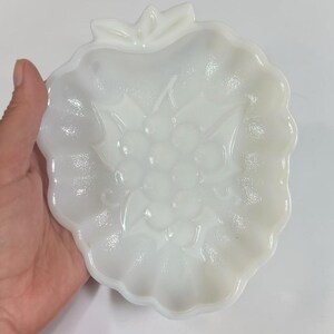 Peut inclure: Un plat en verre opalin blanc en forme de fraise avec un bord festonné. Le centre du plat présente un motif en relief moulé représentant une grappe de baies et de feuilles. La surface a une finition lisse et brillante avec un aspect translucide.
