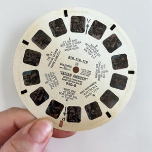 May include: A vintage View-Master reel featuring scenes from "Indian Ambush" with text. The circular reel has multiple small rectangular images and text, including "Rin-Tin-Tin" and "Indian Ambush".