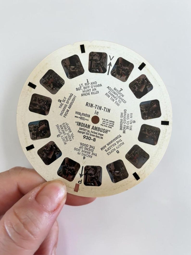 May include: A vintage View-Master reel featuring scenes from "Indian Ambush" with text. The circular reel has multiple small rectangular images and text, including "Rin-Tin-Tin" and "Indian Ambush".