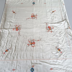 Könnte beinhalten: Eine rechteckige, cremeweiße Tischdecke aus Stoff mit gestickten Motiven von bunten hängenden Laternen und zarten Blütenzweigen. Das Design ist in einem sich wiederholenden Muster angeordnet und von dünnen, orangefarbenen Nähten umrandet.