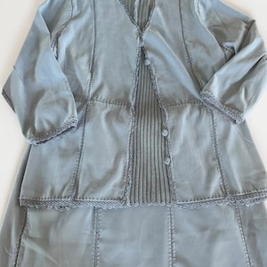 Peut inclure: Un ensemble deux pièces bleu clair composé d'une veste à manches longues et d'une jupe assortie. La veste présente une encolure en V, des boutons et un panneau central côtelé. Les deux pièces ont des coutures décoratives et des bords festonnés.
