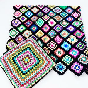 Peut inclure: Une couverture au crochet et un coussin carré assorti présentant un motif de carrés granny colorés. La couverture se compose de carrés multicolores assemblés par du fil noir, tandis que le coussin présente des rangées concentriques de couleurs vives.