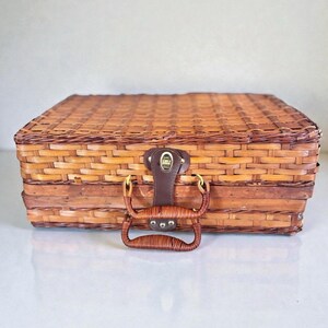 Peut inclure: Un panier de pique-nique rectangulaire en osier tressé marron avec un couvercle plat. Le panier présente une attache en cuir marron foncé avec un accent en métal doré et une poignée incurvée en osier tressé fixée par des ferrures dorées.