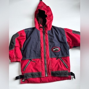 Puede incluir: Chaqueta con capucha roja, azul marino y negra con cremallera completa. La chaqueta presenta un parche con el logotipo en el pecho y detalles negros en las mangas y el dobladillo. Tiene dos bolsillos con cremallera y una capucha.