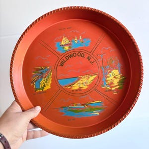 May include: A round, orange serving tray with a rope-like edge. The tray features illustrations of Wildwood, N.J., including sailing, a pier, the beach, and an amusement park. The text "Wildwood, N.J." is in the center.