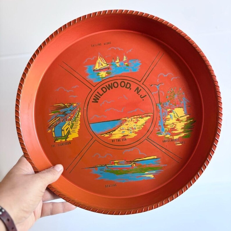 May include: A round, orange serving tray with a rope-like edge. The tray features illustrations of Wildwood, N.J., including sailing, a pier, the beach, and an amusement park. The text "Wildwood, N.J." is in the center.