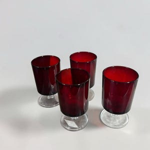 Peut inclure: Un ensemble de quatre verres assortis, chacun doté d'un bol cylindrique rouge rubis profond et d'une base sur pied en verre transparent. Les verres présentent une finition lisse et uniforme ainsi qu'un design simple avec un pied robuste.