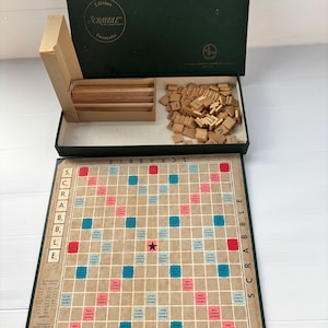 Pode incluir: Conjunto de jogo de tabuleiro Scrabble vintage. O tabuleiro é bege com uma grelha de quadrados coloridos. O conjunto inclui peças de letras de madeira, um suporte de madeira para peças e uma caixa verde escura com a inscrição "Edition Scrabble Française".
